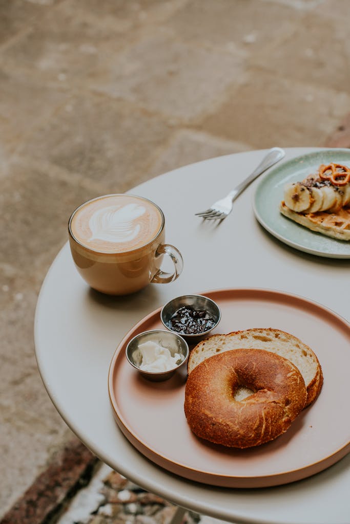 A cozy cafe breakfast scene featuring a bagel with spreads and a coffee latte.