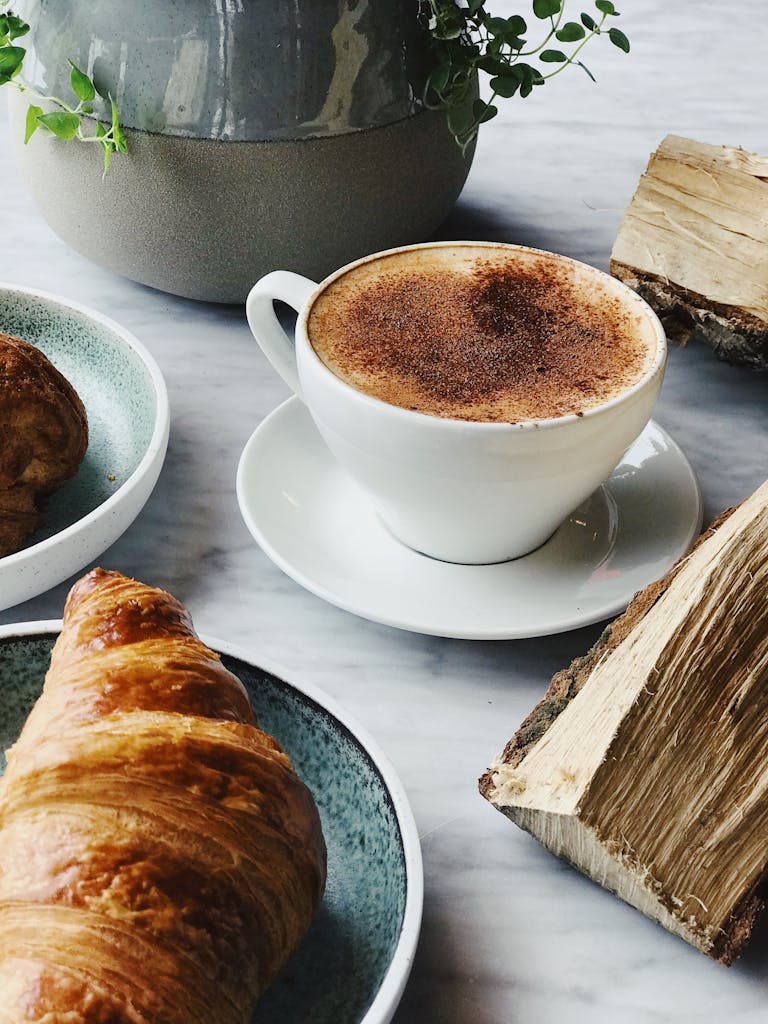 Close-up of a steaming cappuccino with a golden croissant, perfect for a cozy morning.